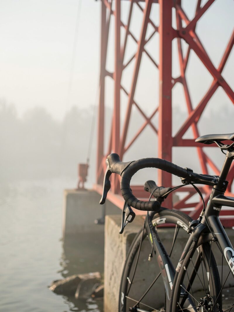 A small group of cyclists gathering at the north end of the Golden Gate Bridge at dawn, red tower rising into fog, blinky lights and helmets