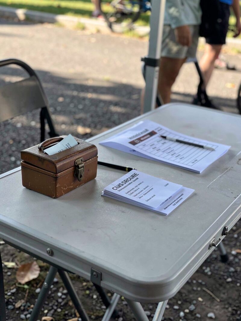 A folding table with a small cash box, a roster sheet and blank membership cards at a club ride sign-in, morning light